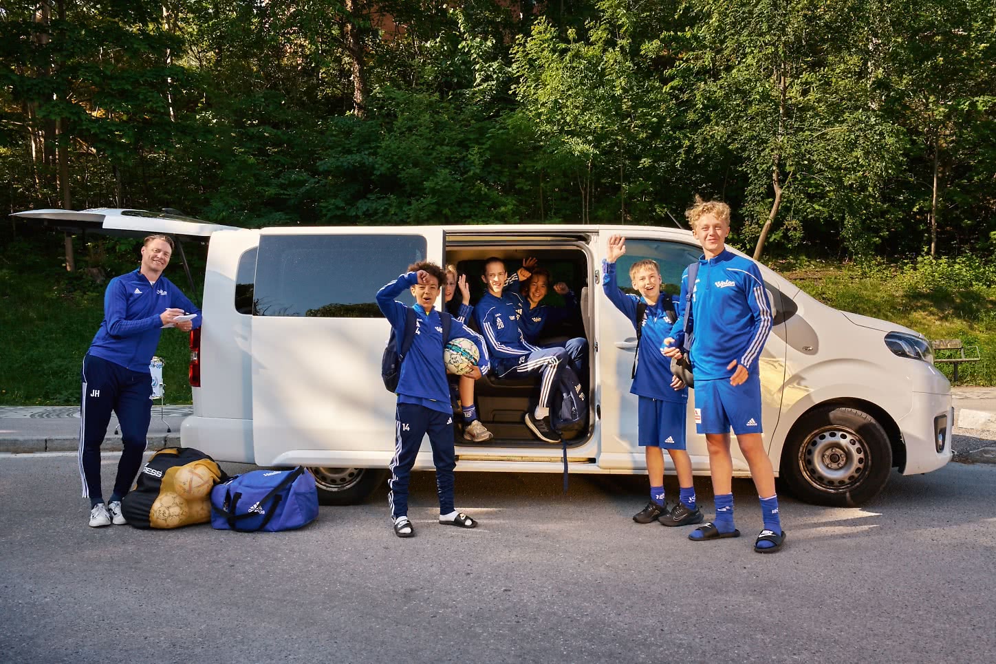 Ett ungdomslag i träningskläder står vid en minibuss inför avfärd till match eller turnering.